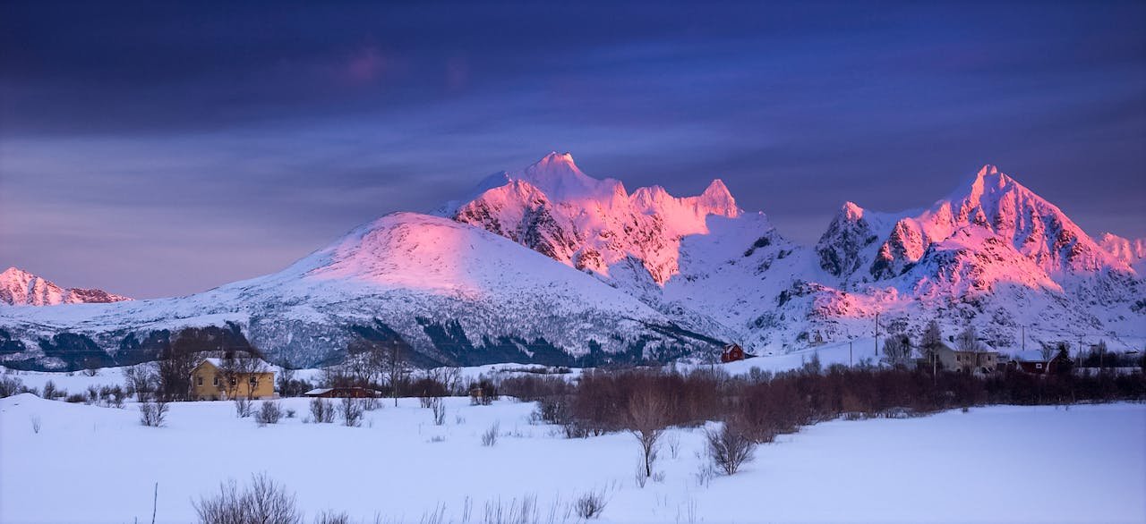 Majestic snow-covered mountains in Lofoten, Norway at sunset with pink glow and serene landscape.